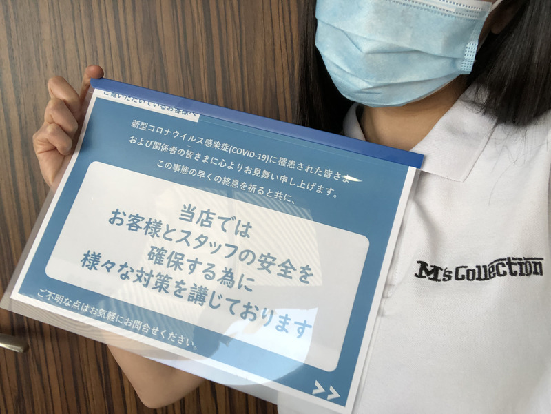 マスクを着用したスタッフがコロナ対策の案内カードを手に持って撮影した写真
