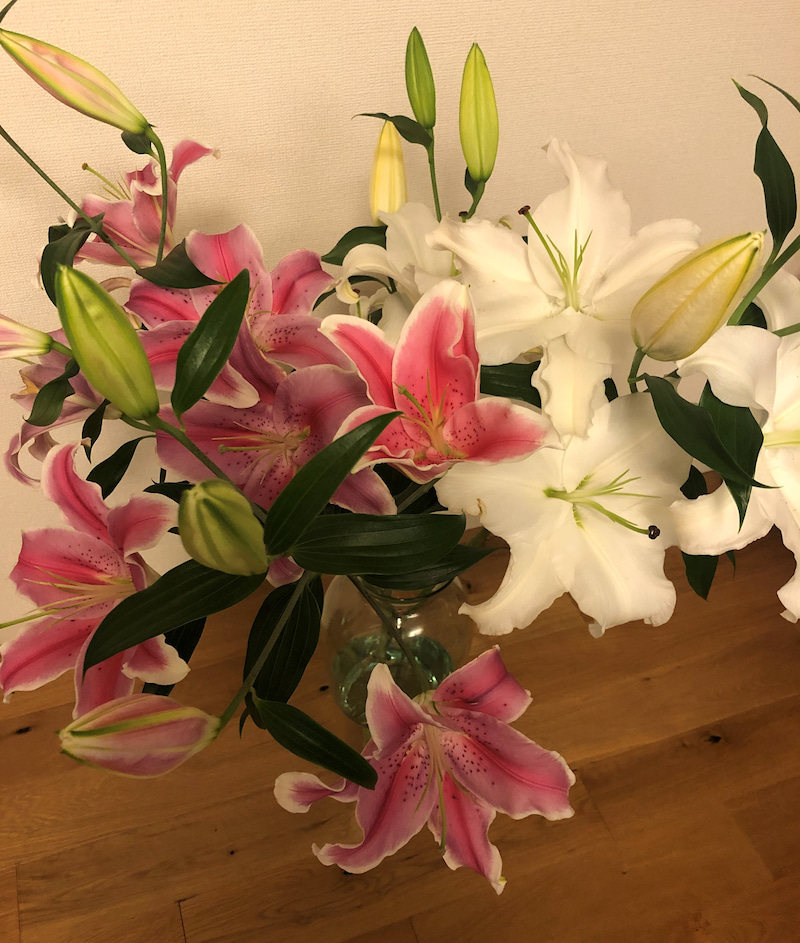 木目調の床に置かれたピンクと白のユリの花束を撮影した写真