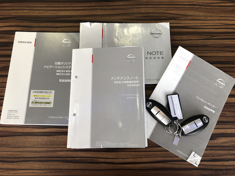 取扱説明書とメンテナンスノート、スマートキーを木目調のテーブルに並べて撮影した写真
