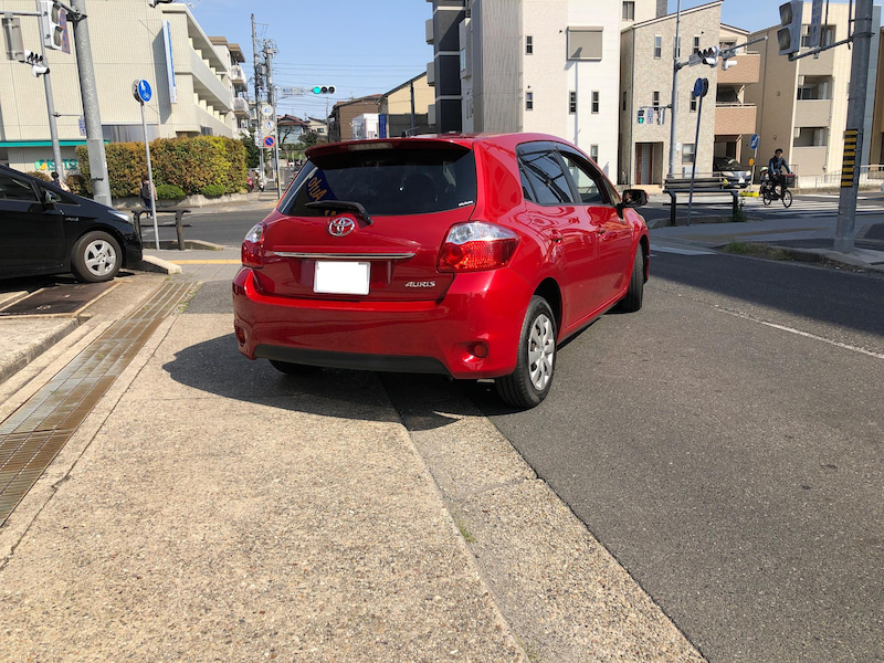 赤いトヨタオーリスを道路上で斜め後方から撮影した外観写真