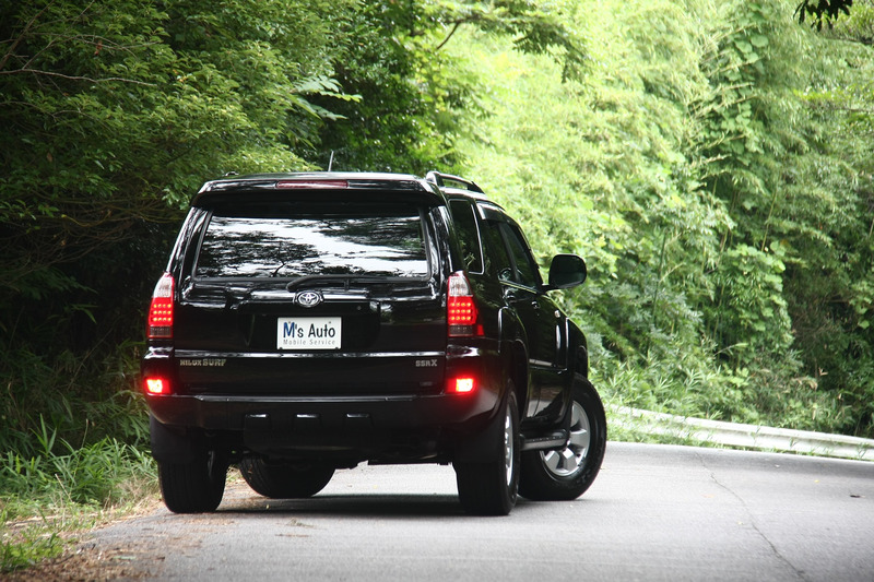 森の中の道路で黒のハイラックスサーフをブレーキランプ点灯状態で背面から撮影した外観写真