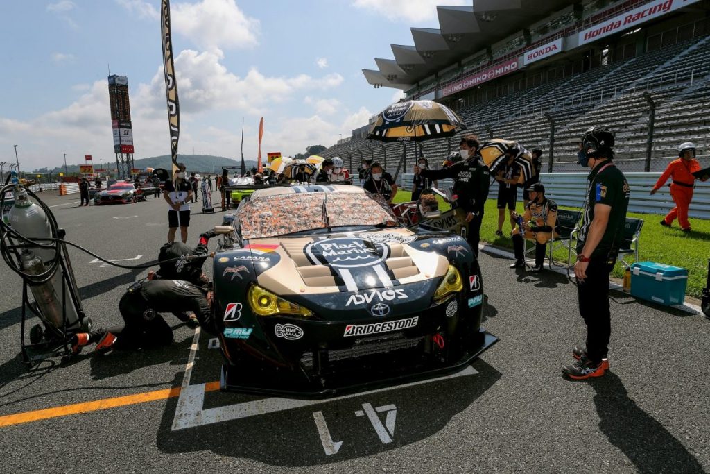 ピットでスタッフに囲まれた金色のADVICSレースカーを撮影した写真