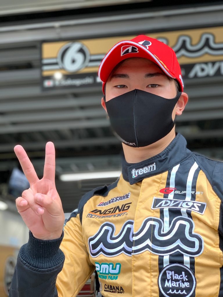 レーシングスーツ姿のドライバーがピースサインをする写真