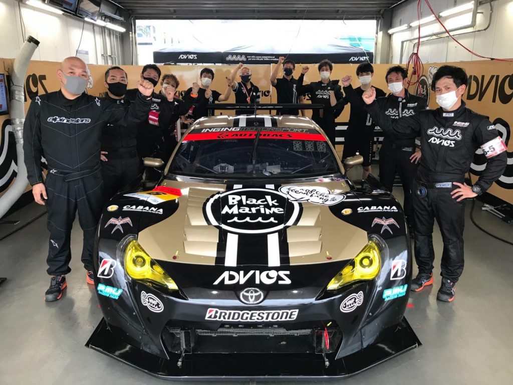ポールポジション獲得を喜ぶチーム全員と黒いレースカーの記念写真