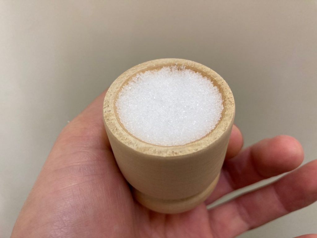 手のひらに乗せた木製容器に入った塩を撮影した写真