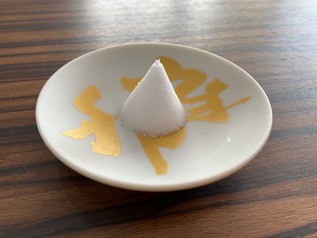 金文字模様の小皿に盛られた円錐形の塩を撮影した写真