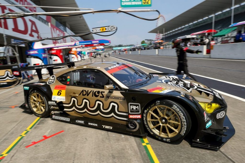 ピットレーンに停まる金色のADVICSレースカーを側面から撮影した写真