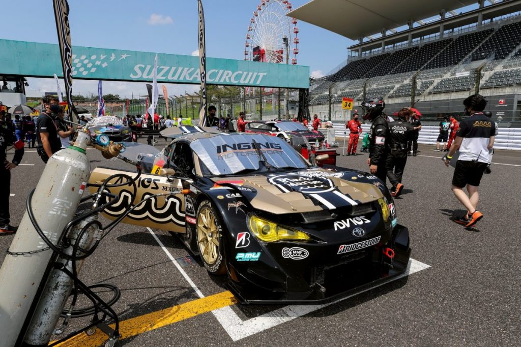 鈴鹿サーキットのピットで金色のADVICSレースカーを整備するチームスタッフ