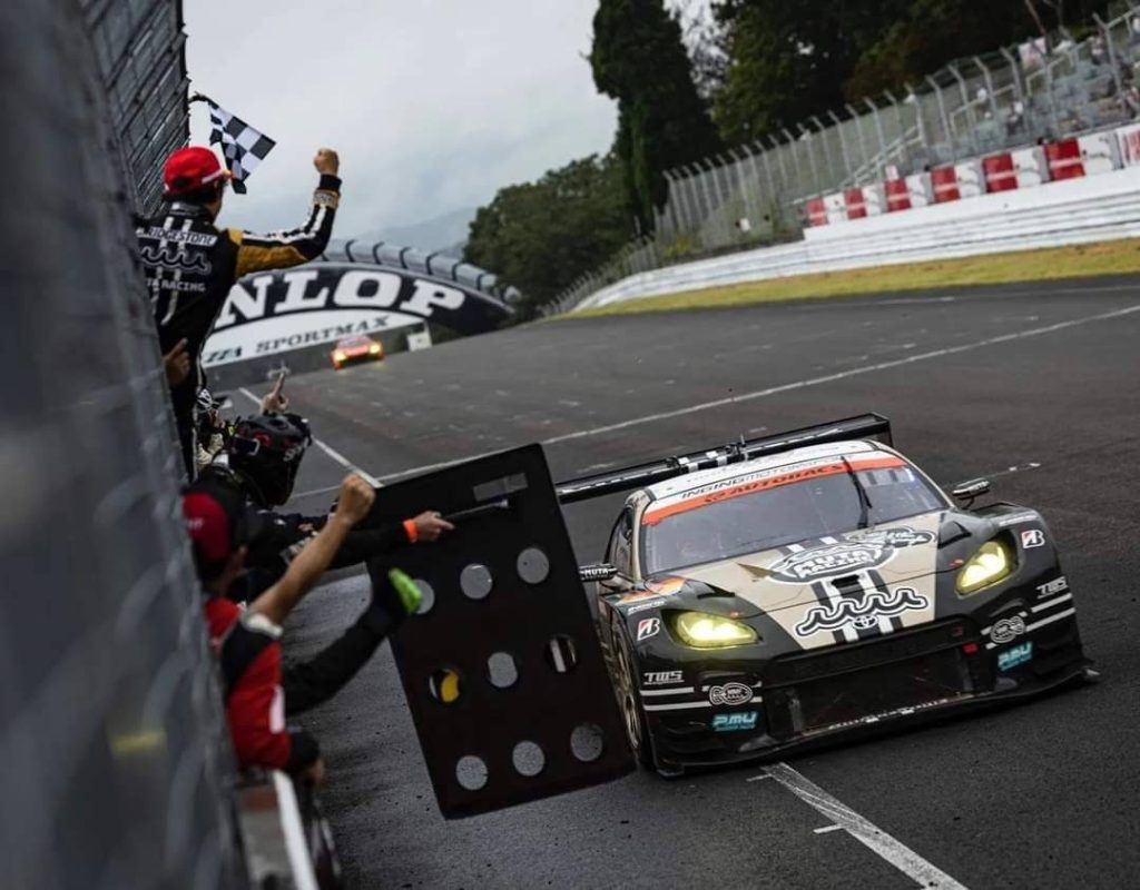 菅生サーキット300kmレースでのピットクルーと走行中のレースカーのサーキットシーン